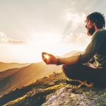Man meditating yoga lotus pose at sunset mountains Travel Lifestyle relaxation emotional concept summer vacations outdoor harmony with nature calm scene